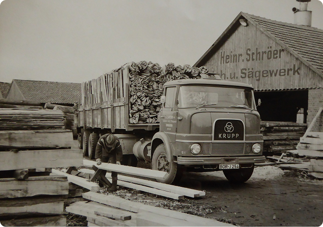 Historische Aufnahme des Schröer Sägewerks in Dingden: Ein Krupp-Lkw wird mit Holz beladen, Arbeiter im Einsatz, Gebäude mit der Aufschrift „Heinr. Schröer Sägewerk“ – zeigt die lange Tradition und handwerklichen Ursprung von Holz-Schröer.